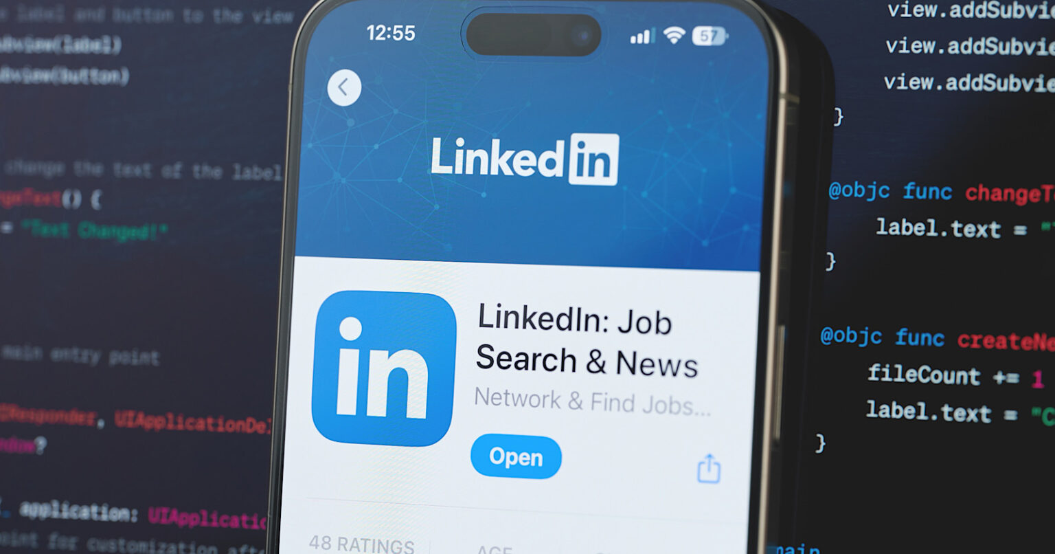 LinkedIn app on a smartphone screen with a background of computer code, highlighting profile enhancement and networking features for in-demand skills.