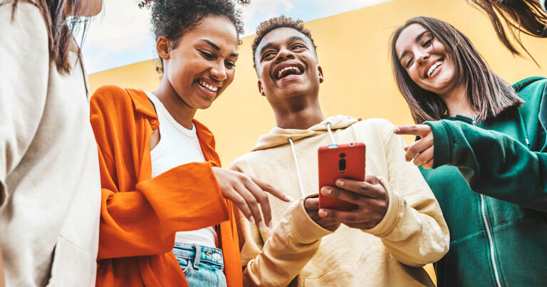 A diverse group of Gen Z friends laughing and looking at a smartphone held by a young man, outdoors under a bright, colorful background.