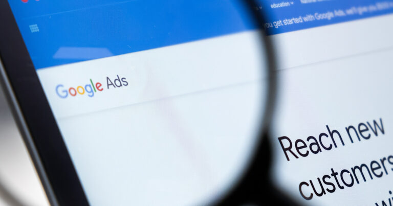 Close-up view of a computer screen displaying "Google Ads" with a magnifying glass focusing on the text "reach new customers.