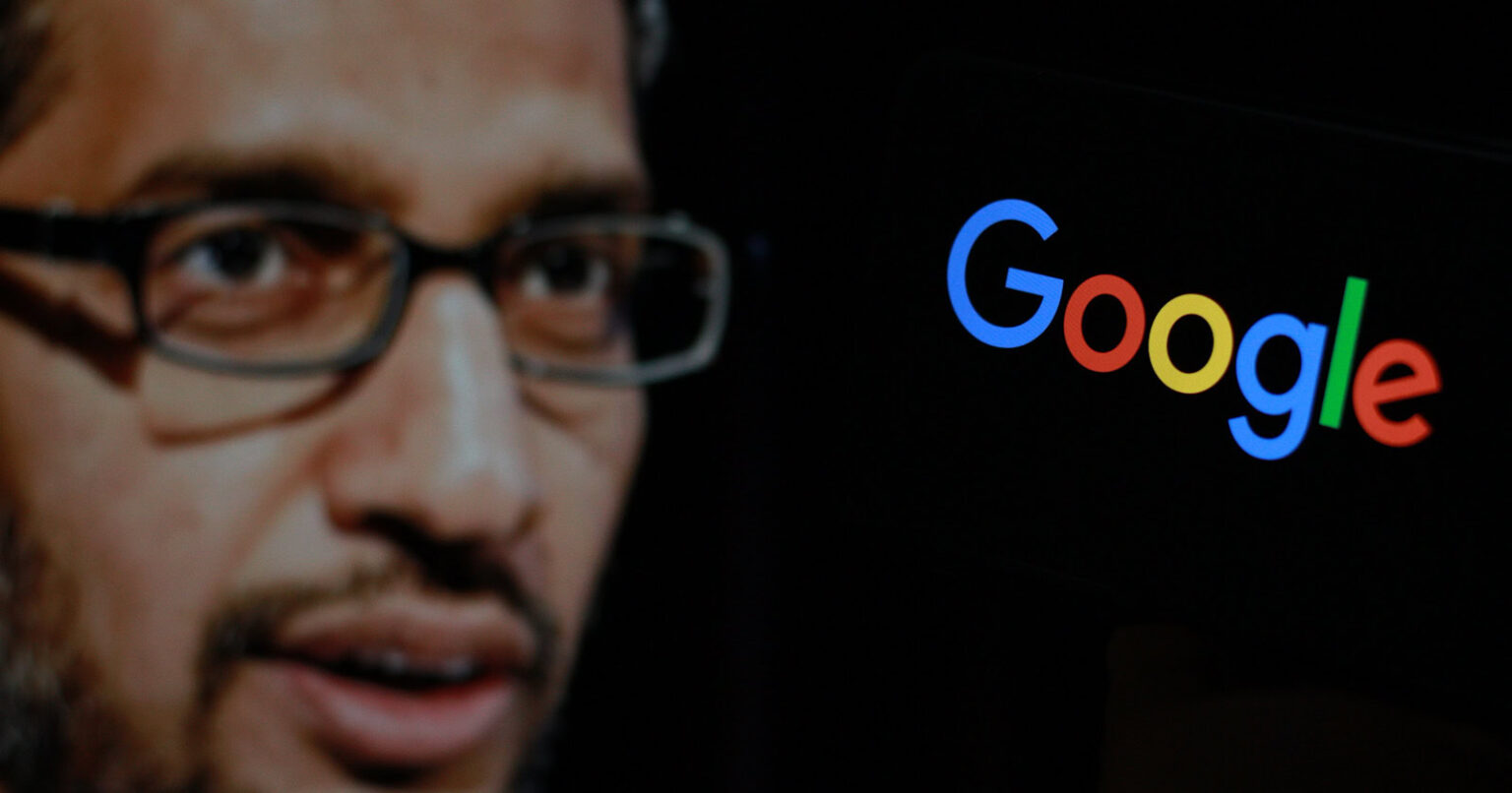 In this photo the Google logo is displayed on the smartphone screen with CEO Sundar Pichai in the background.