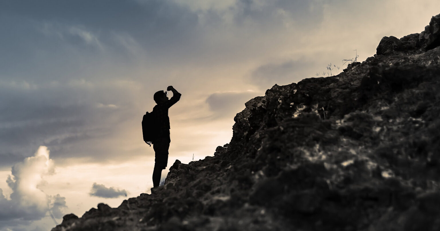 Man getting ready to climb up mountain looking up at the challenge before him planning path.